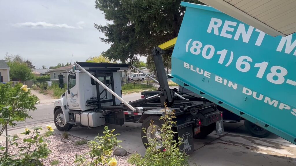 A truck dropping off a blue dumpster on a residential driveway for Blue Bin Dumpster Rentals in Salt Lake City, UT.
