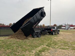 A Trademark Dumpsters trailer dumping soil, demonstrating landscaping waste removal services in Wilmington, DE.
