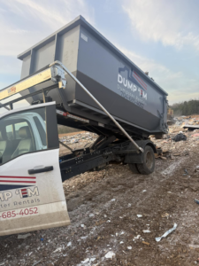 A Dump 'Em Dumpster Rentals truck emptying a dumpster at a landfill or waste site in Charlotte, NC.