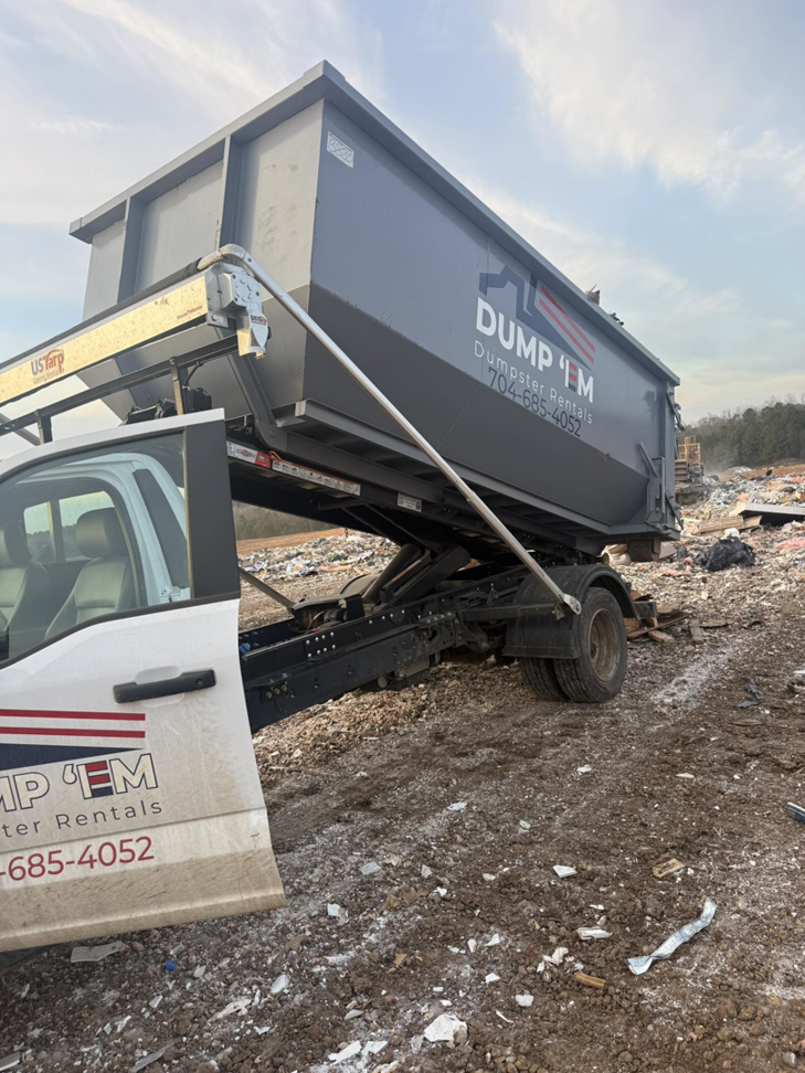 A Dump 'Em Dumpster Rentals truck emptying a dumpster at a landfill or waste site in Charlotte, NC.