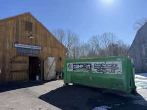 A green Dump-It Dumpster Rentals dumpster placed in front of a barn at Wethering Heights Farm in Concord, NH.