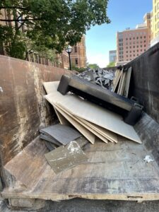 A large dumpster filled with construction debris, including wood and tiles, indicating a junk removal project by Prestige Junk Removal & Hauling in Detroit, MI.