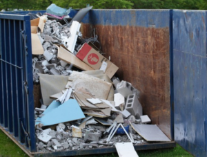 A large blue dumpster filled with construction and demolition debris, ready for removal by The Dumpster Guy in Webster, MA.