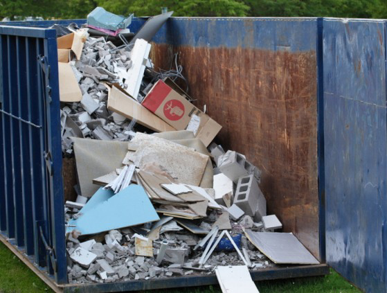 A large blue dumpster filled with construction and demolition debris, ready for removal by The Dumpster Guy in Webster, MA.