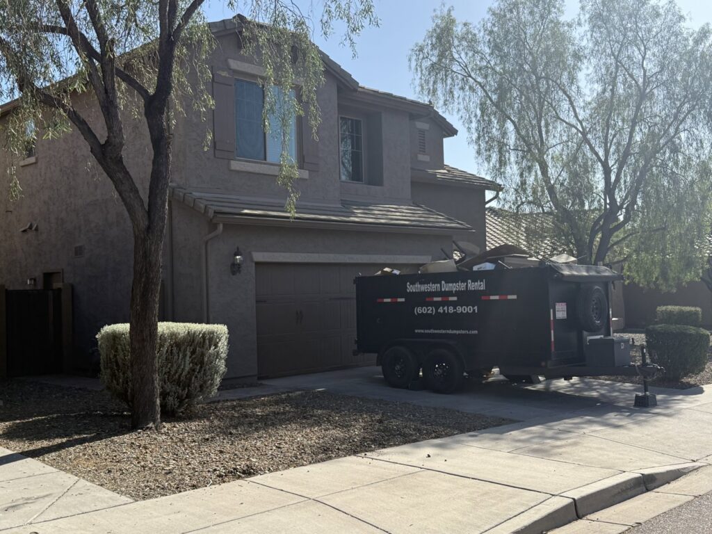 A black dumpster trailer from Southwestern Dumpster Rental and Junk Removal, partially filled with debris, parked in a residential driveway in Peoria, AZ.