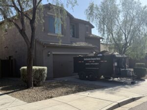 A black dumpster trailer from Southwestern Dumpster Rental and Junk Removal, partially filled with debris, parked in a residential driveway in Peoria, AZ.