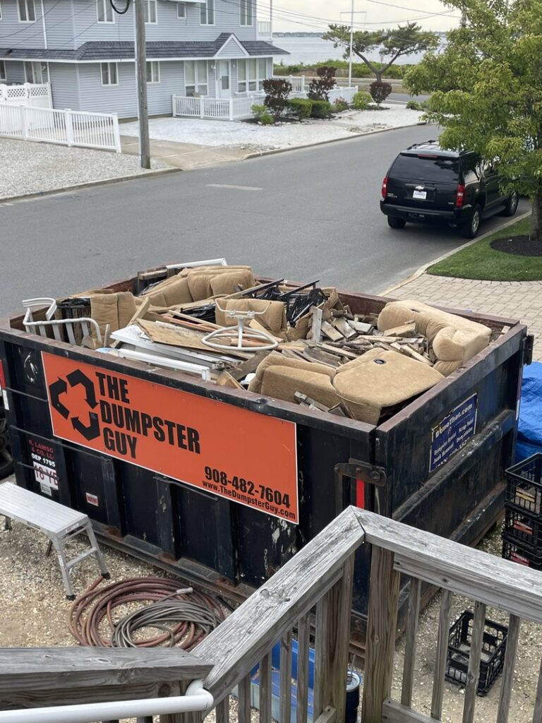 A roll-off dumpster from The Dumpster Guy, filled with old furniture and debris at a residential location in Webster, MA.