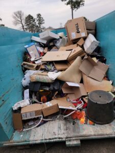 A blue dumpster filled with cardboard boxes and household junk for removal by Site Boss Dumpster Rentals in Raeford, NC.