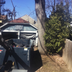 A Chet's Disposal dumpster filled with junk next to a residential garage in Springfield, MA.