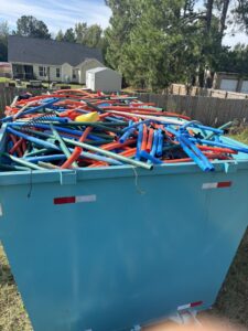 A blue dumpster filled with colorful pool noodles and pipes for junk removal by Site Boss Dumpster Rentals in Raeford, NC.