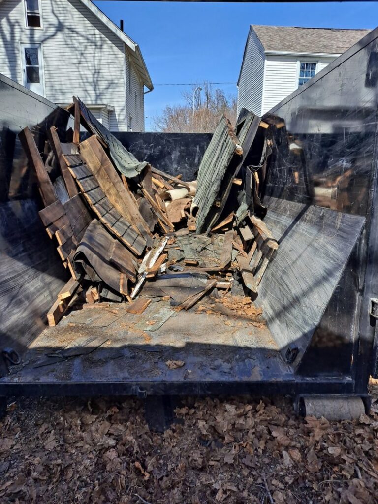 A dumpster from TRS Roll-Offs LLC filled with old roofing shingles and wood, showing demolition debris removal in Canton, OH.
