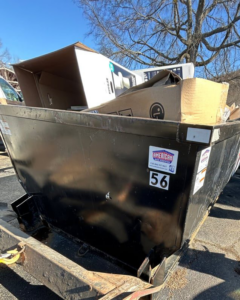 A black dumpster on a trailer filled with cardboard boxes and other waste, used for junk removal by HD Waste Services in Chattanooga, TN.