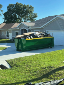 A green dumpster filled with construction debris and trash bags on a residential driveway by Wastecon in Harrisburg, PA.