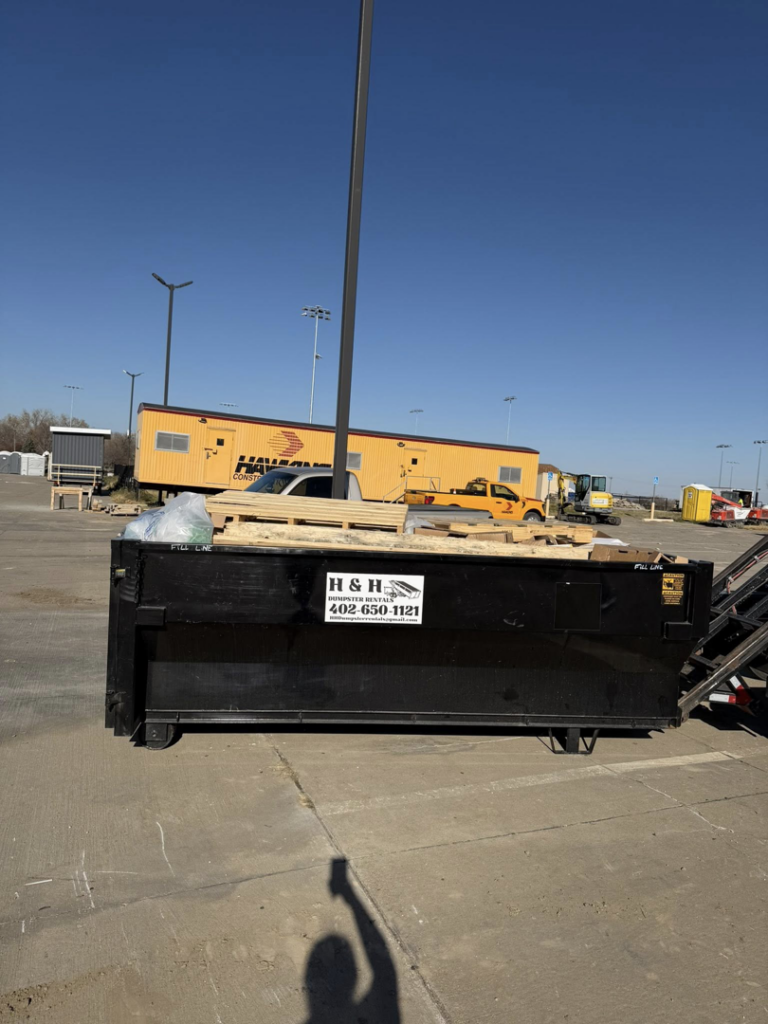 An H & H Dumpster Rental dumpster partially filled with wood debris at a commercial site in Rootstown, OH.