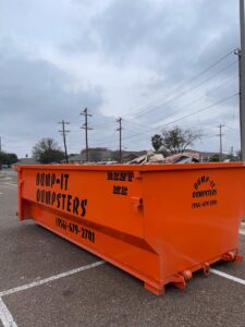 An orange Dump-IT Dumpster Rentals LLC dumpster partially filled with debris, indicating a junk removal job in Laredo, TX.