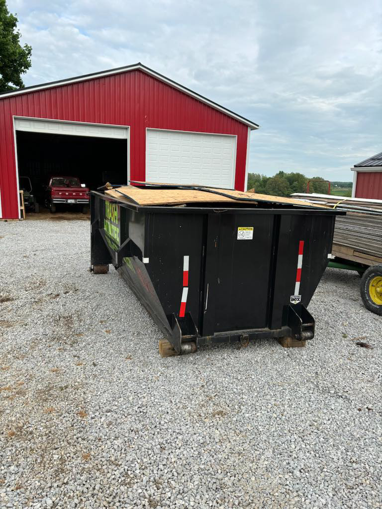 A Trash Hunter LLC dumpster partially filled with construction debris next to a red barn in Hartville, OH.
