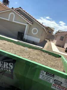A green dumpster from Junk Control filled with dirt and rock debris at a residential property in Henderson, NV.