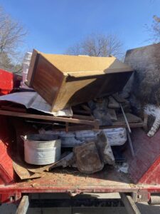 A roll-off dumpster filled with household debris, including a cabinet and mattresses, collected by Jedi Junk Removal Garbage Services Pocatello, ID.