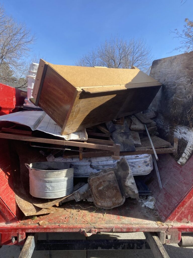 A roll-off dumpster filled with household debris, including a cabinet and mattresses, collected by Jedi Junk Removal Garbage Services Pocatello, ID.