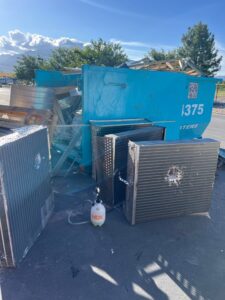A blue dumpster filled with various junk items, including old AC units and metal, for Blue Bin Dumpster Rentals in Salt Lake City, UT.