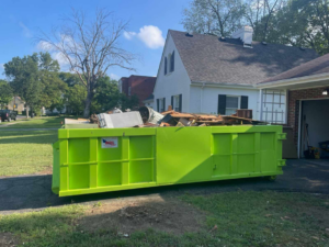 A large green dumpster filled with household junk and debris in a residential driveway from Pack Mule Dumpsters Dayton, OH.