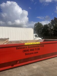 A red dumpster from Vetcans Dumpster Rental filled with cardboard and debris, ready for junk removal in Jacksonville, FL.
