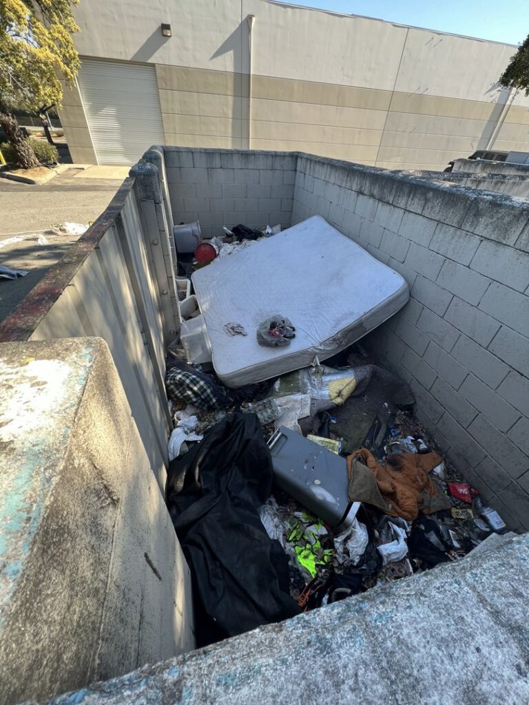 A large dumpster overflowing with a mattress and various trash items, ready for removal by Sac Junk in Rancho Cordova, CA