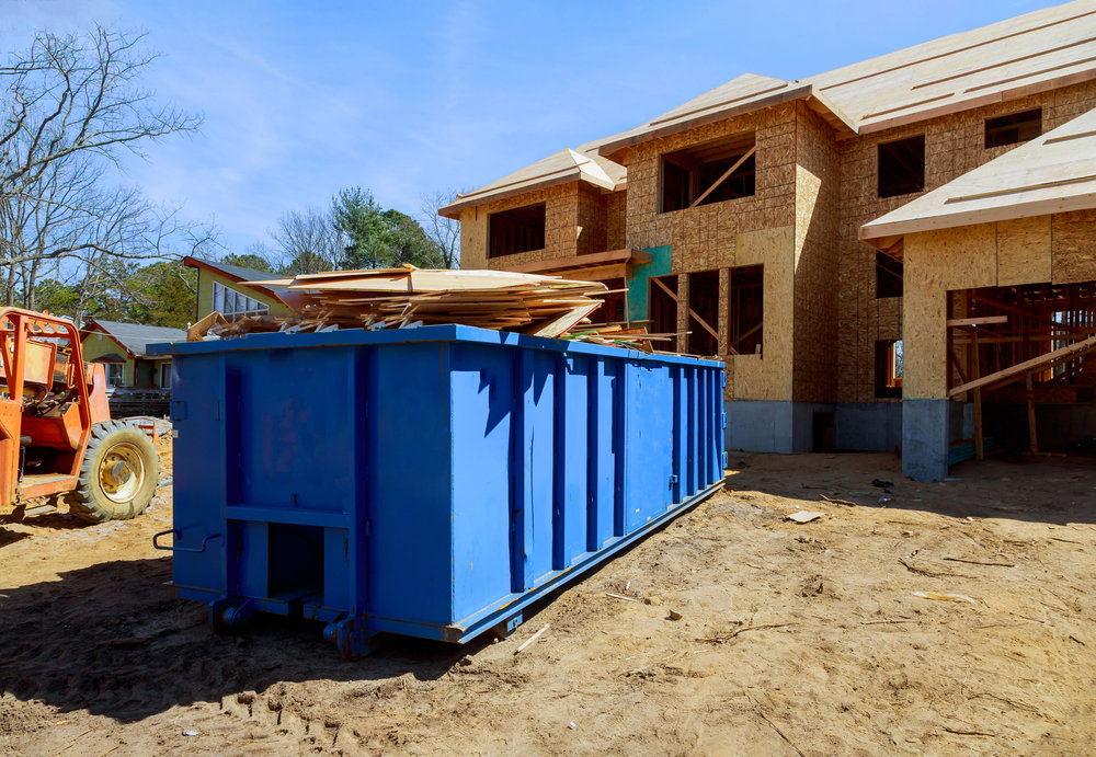 A blue roll-off dumpster filled with wood and construction debris at a job site, provided by Dumpster 360 in Clarksville, TN.