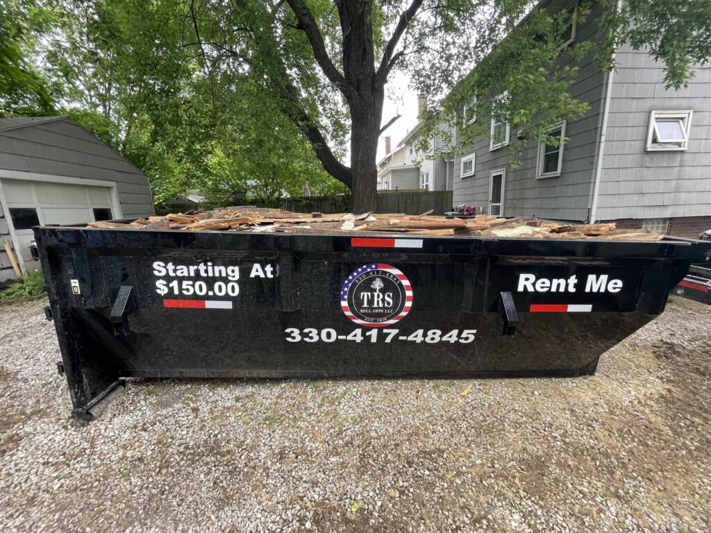 A black dumpster from TRS Roll-Offs LLC filled with wood debris, showcasing a junk removal service in Canton, OH.