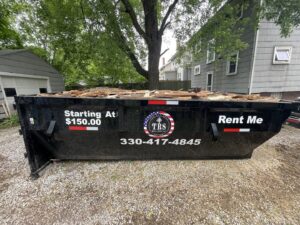 A black dumpster from TRS Roll-Offs LLC filled with wood debris, showcasing a junk removal service in Canton, OH.