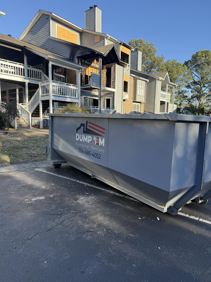 A Dump 'Em Dumpster Rentals dumpster placed in front of a fire-damaged apartment building in Charlotte, NC.