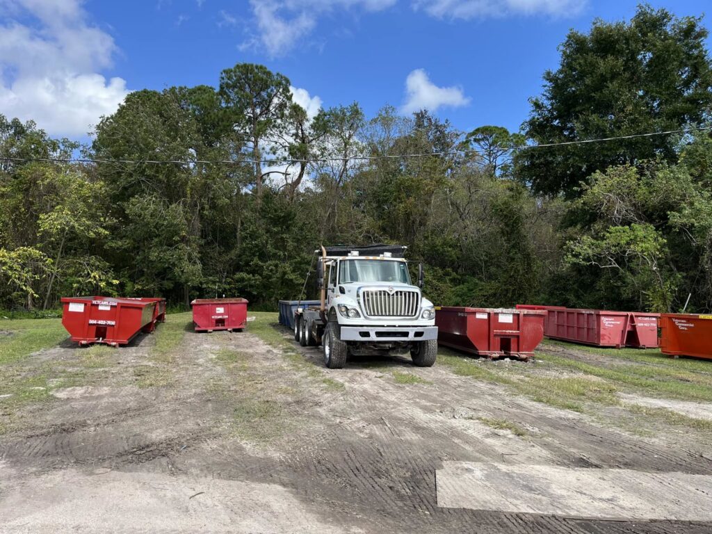 A Vetcans Dumpster Rental truck parked among several red dumpsters in a dirt lot in Jacksonville, FL.