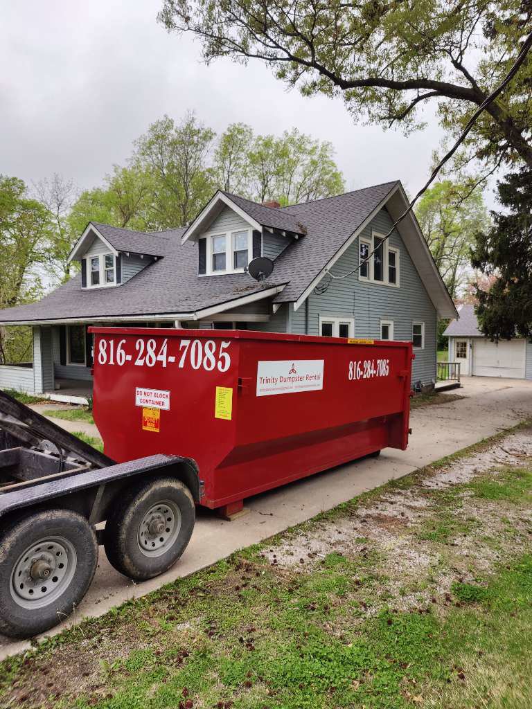 A red dumpster from Trinity Dumpster Rental LLC for debris removal at a residential site in Kansas City, MO.