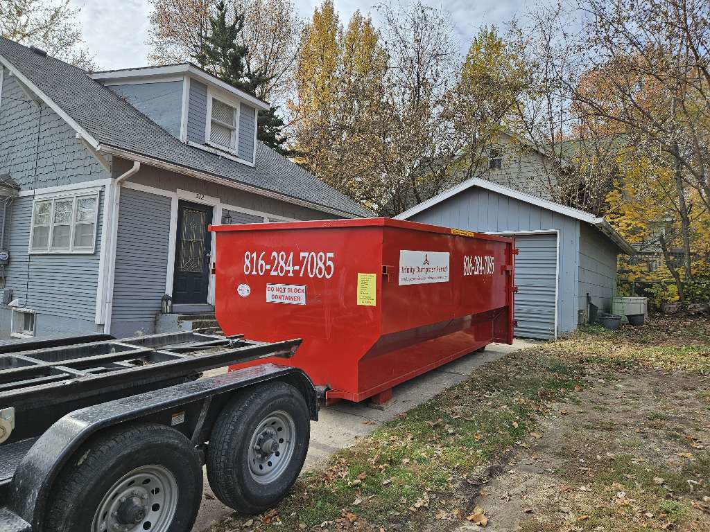 A red dumpster from Trinity Dumpster Rental LLC ready for junk removal at a residential property in Kansas City, MO.