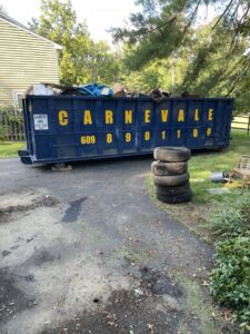 An AJ Carnevale Disposal dumpster filled with household junk and old tires on a driveway in Hamilton, NJ
