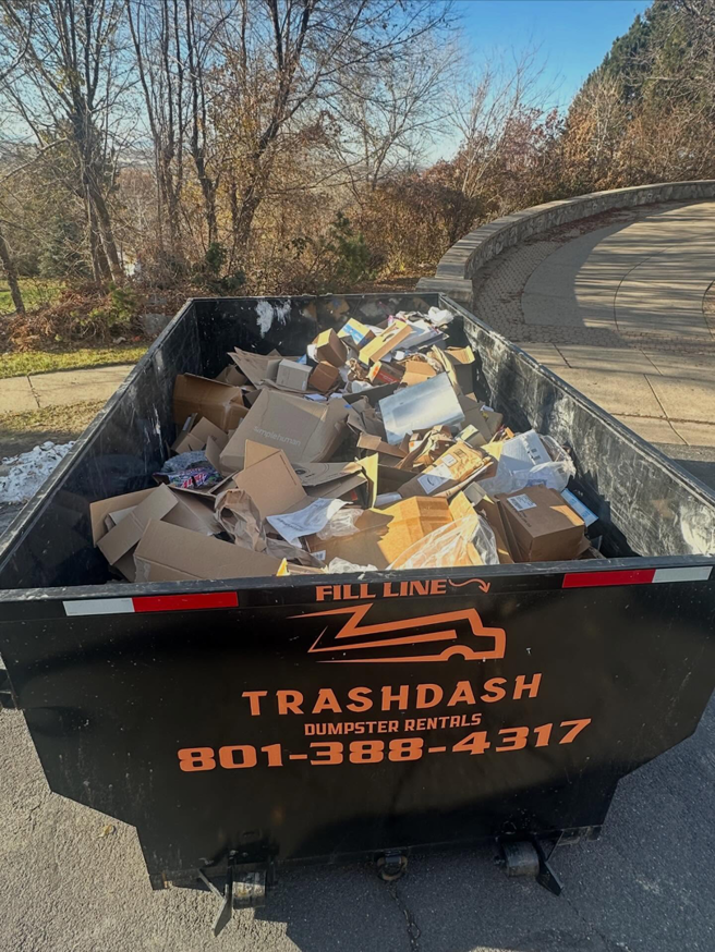 A TrashDash dumpster filled with numerous cardboard boxes and packaging materials in West Haven, UT.