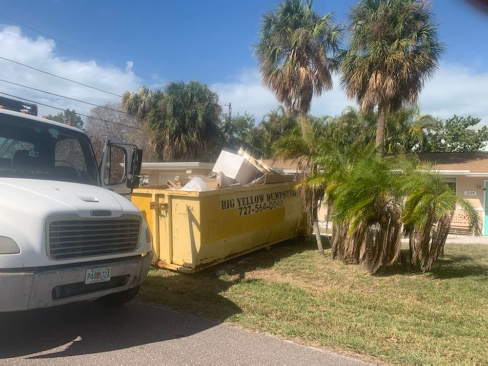 A Big Yellow Dumpster full of construction debris next to a residential house in Saint Petersburg, FL, for a general contractor job.