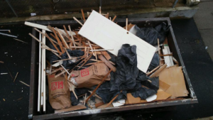 A large dumpster filled with construction debris, wood, and trash bags by R & J Junk Removal in Warwick, RI.