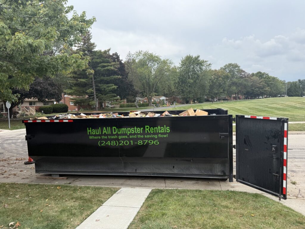 A large black dumpster full of construction debris and household junk, provided by Haul All Dumpsters in Sterling Heights, MI.