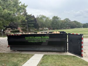 A large black dumpster full of construction debris and household junk, provided by Haul All Dumpsters in Sterling Heights, MI.
