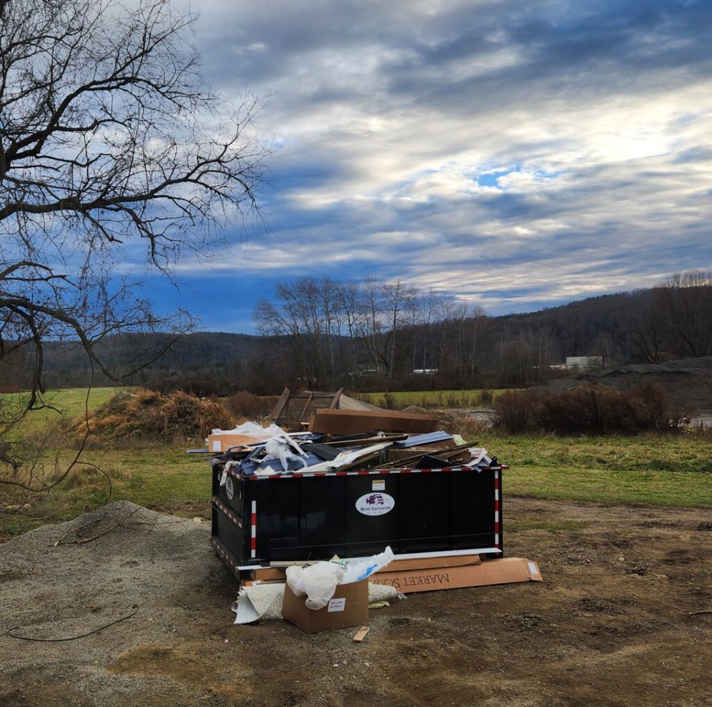 A black roll-off dumpster from Wint Services, LLC, filled with construction debris and junk on an outdoor site in Colorado Springs, CO.