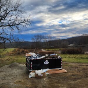 A black roll-off dumpster from Wint Services, LLC, filled with construction debris and junk on an outdoor site in Colorado Springs, CO.
