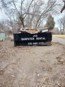 A J & A Haul Away & Dumpster Rentals black dumpster filled with old furniture and debris in Derby, KS.