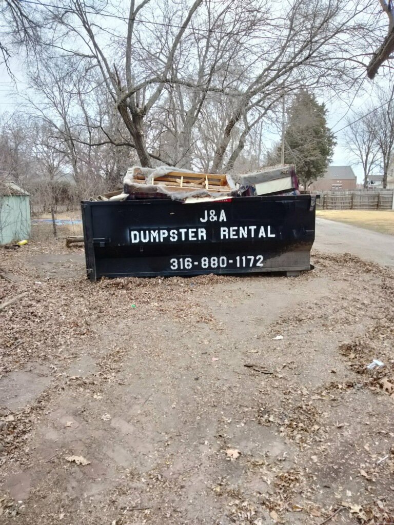 A J & A Haul Away & Dumpster Rentals black dumpster filled with old furniture and debris in Derby, KS.