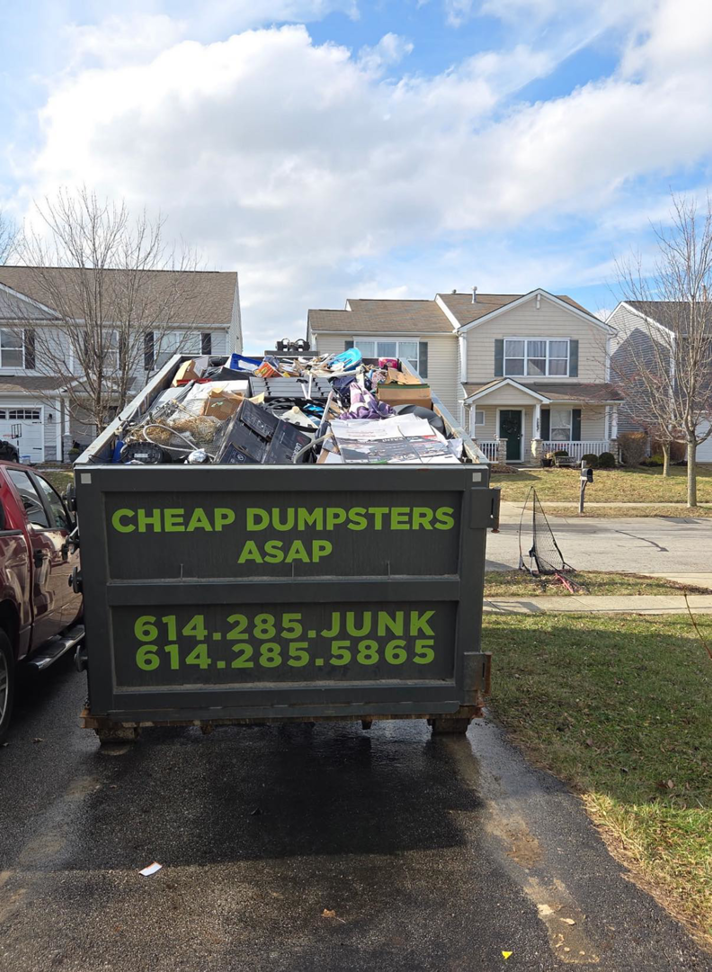 A dumpster filled with various household junk in a residential driveway for removal by Cheap Dumpsters ASAP in Columbus, OH.