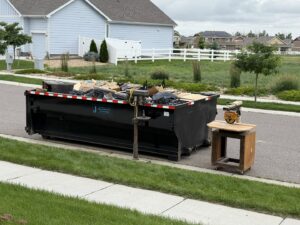 A Blue J's Services Dumpster Rental container filled with junk and debris on a residential street in Greeley, CO, during a cleanup.