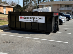 A black dumpster full of various junk items, including a mattress, provided by The Junk Ninjas in Hampton Roads, VA.