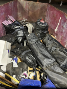 A large dumpster filled with black trash bags, cardboard, and various debris, ready for hauling by Discount Hauling in Las Cruces, NM.
