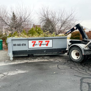 A Triple 7 Dumpsters roll-off dumpster filled with yard waste and branches, ready for removal in Ogden, UT.