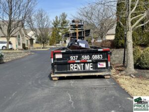A dumpster filled with residential junk and old furniture on a driveway in Dayton, OH, from Big Reds Dumpster Rental.